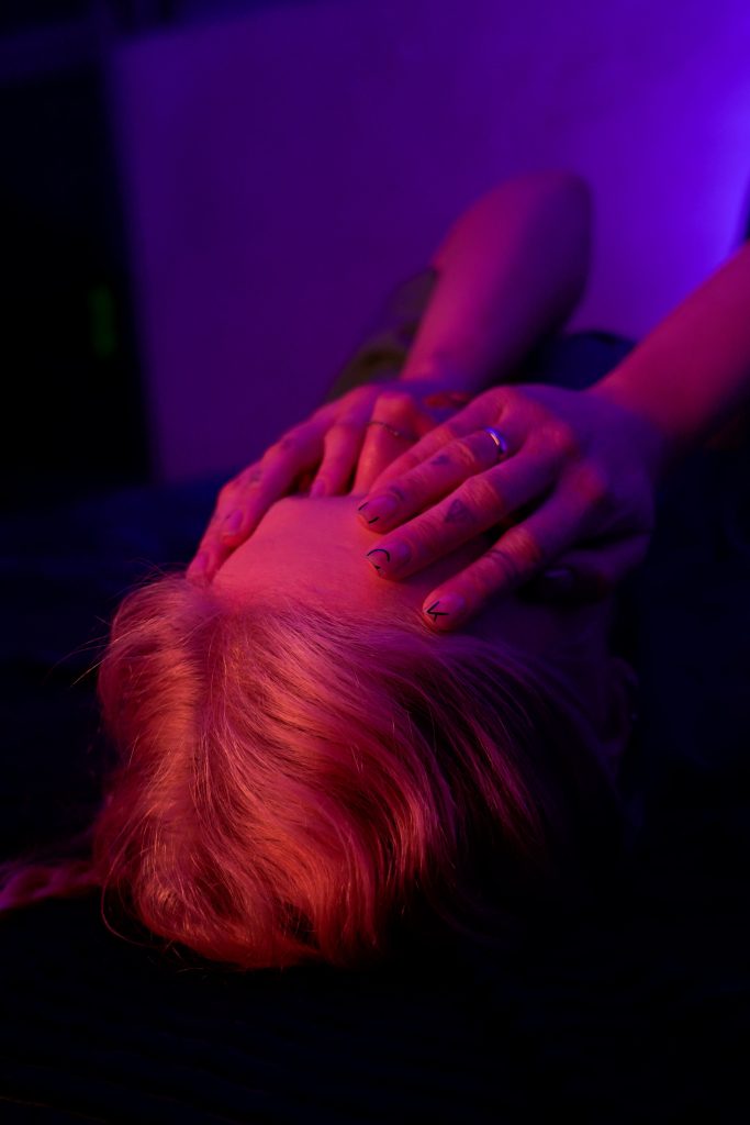 A person with hands covering face under dramatic pink and purple neon light, evoking deep emotion.